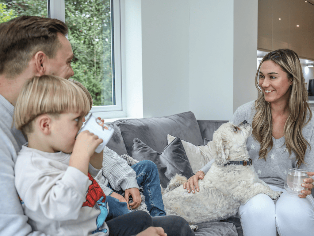 two parents sat on a couch with the dad holding their son drinking from a cup